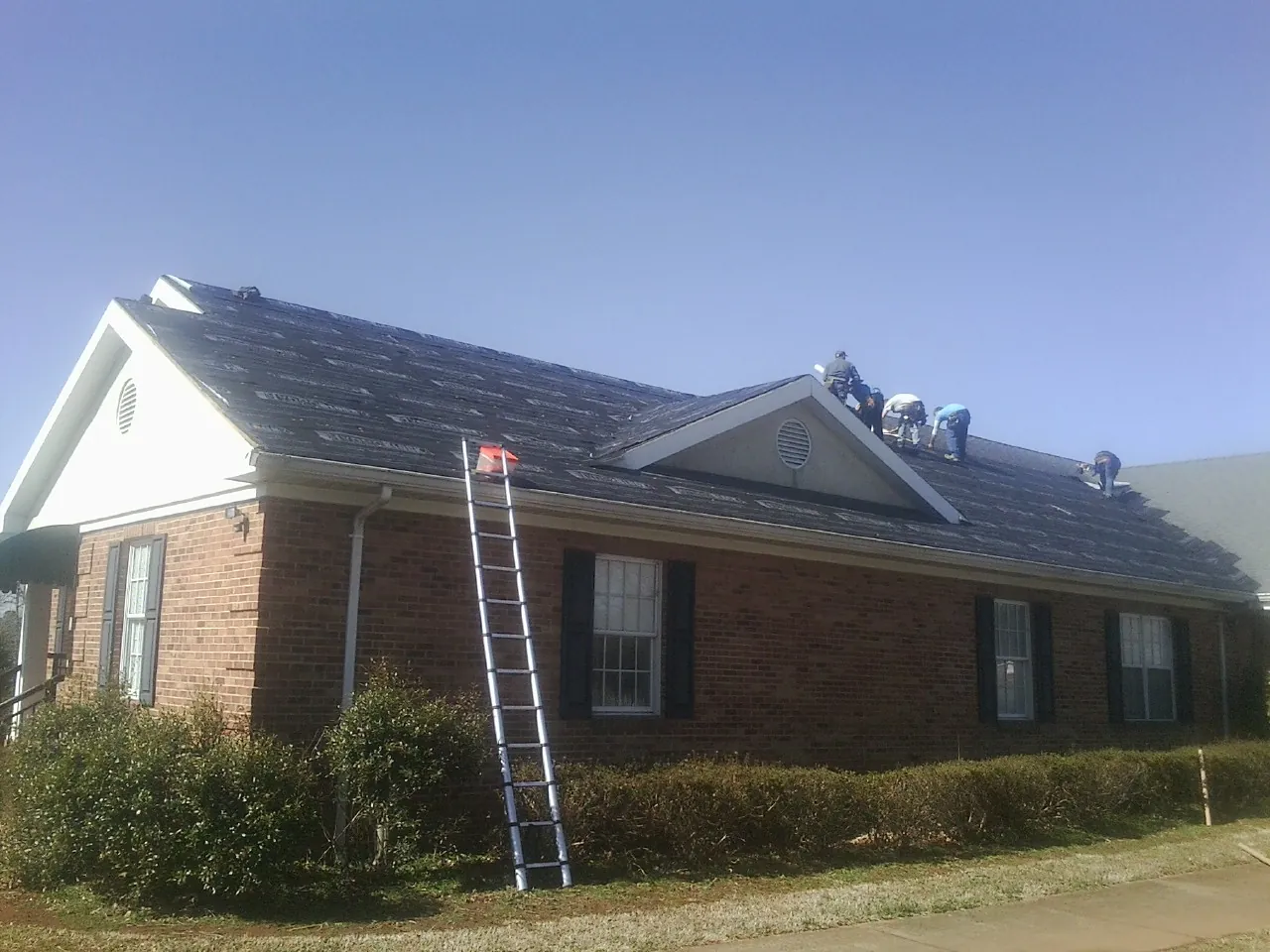 Crew tearing shingles off a brick ranch roof with a ladder set — Emergency Roof Repair work by our crew in Haw River