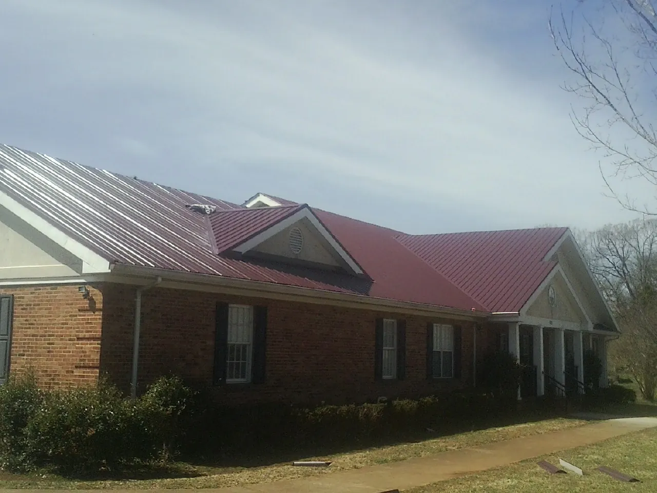 Red metal roof with gabled entries on a long brick building, from a Hail Damage Roof Repair job in Haw River