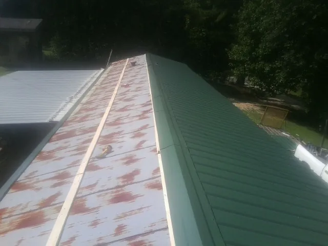 Old rusted panels beside newly installed green metal roofing — Wind Damage Roof Repair by Roofing Brothers in Haw River