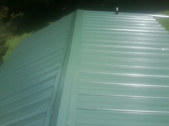 New green metal panels meeting at the ridge of a roof — Flat Roof Repair work by our crew in Haw River