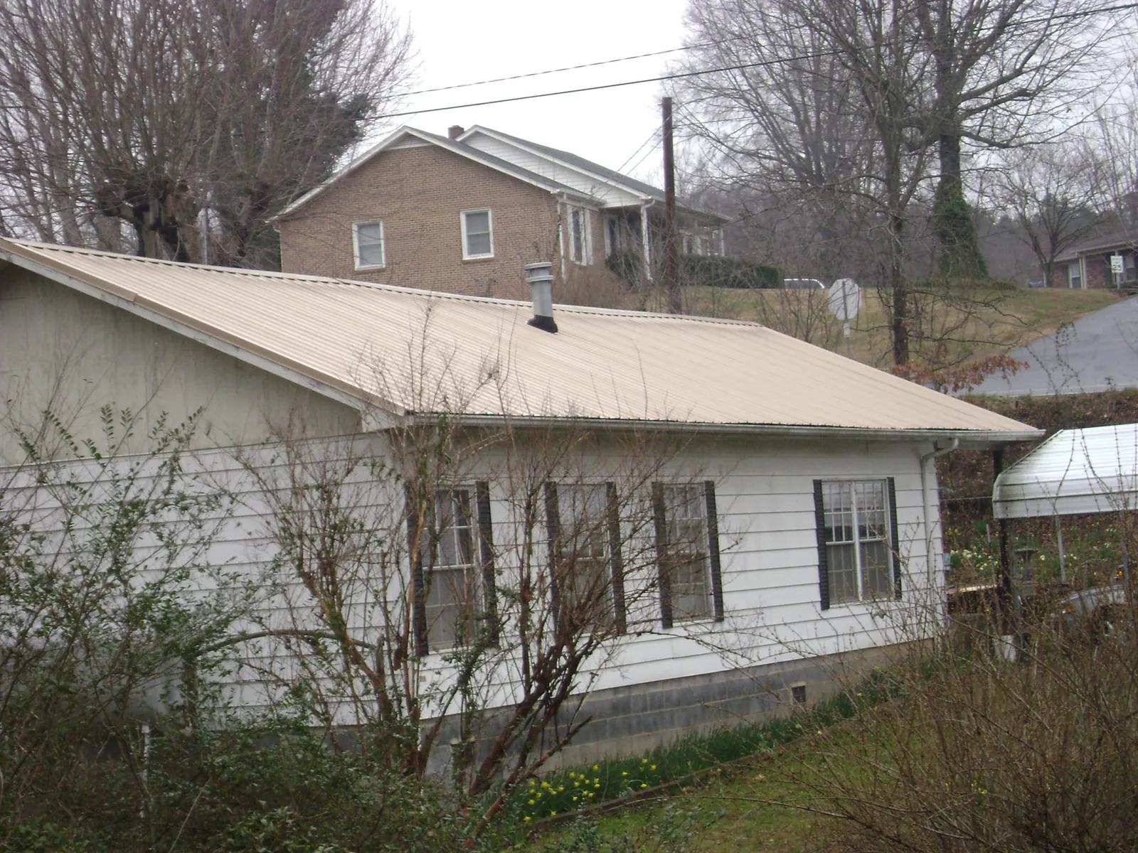 Tan metal roof on a white sided house set into a hillside — Commercial Roofing by Roofing Brothers in Haw River