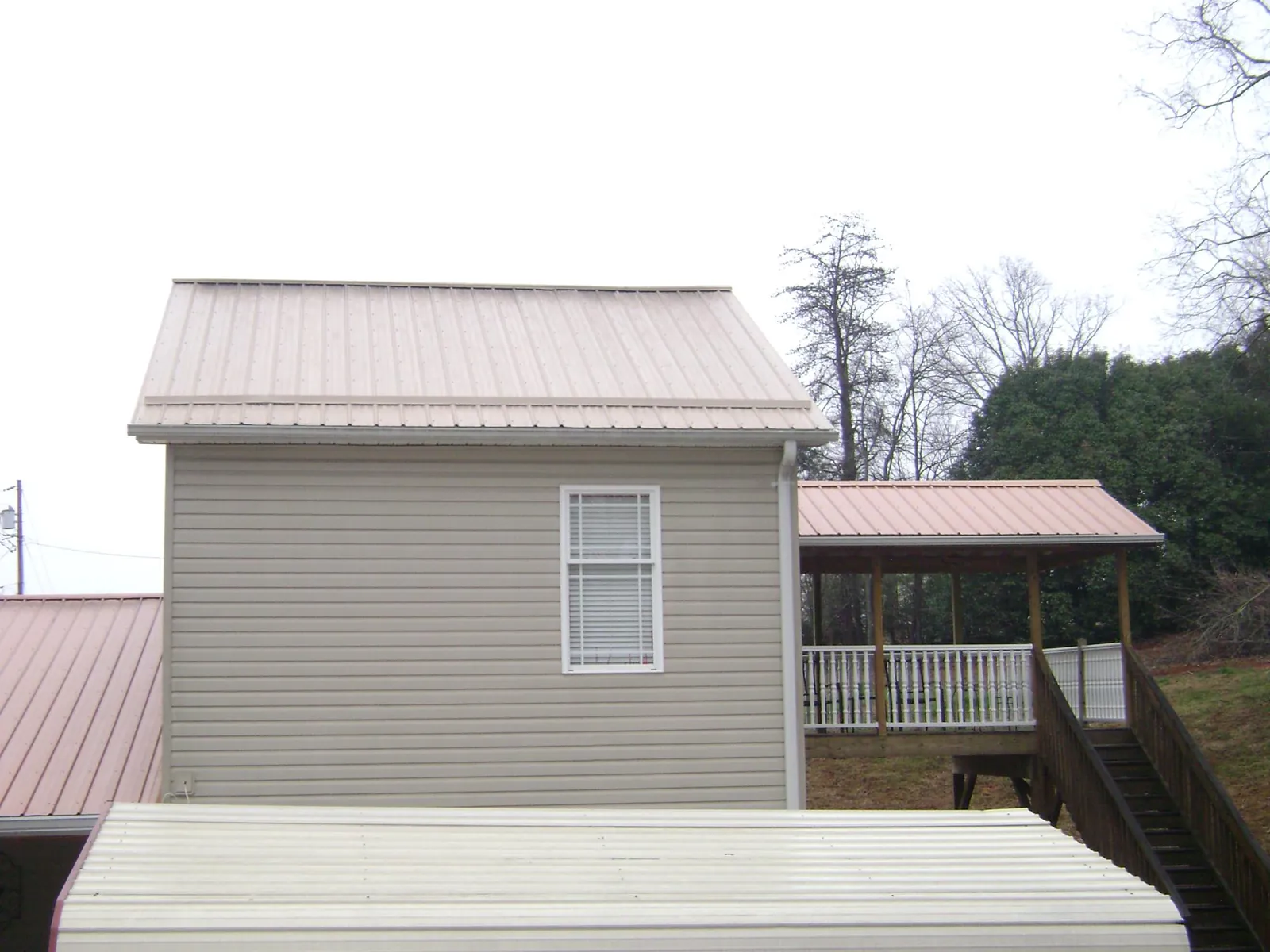 Tan metal roofs on a two story addition and attached porch, from a Roof Replacement job in Haw River